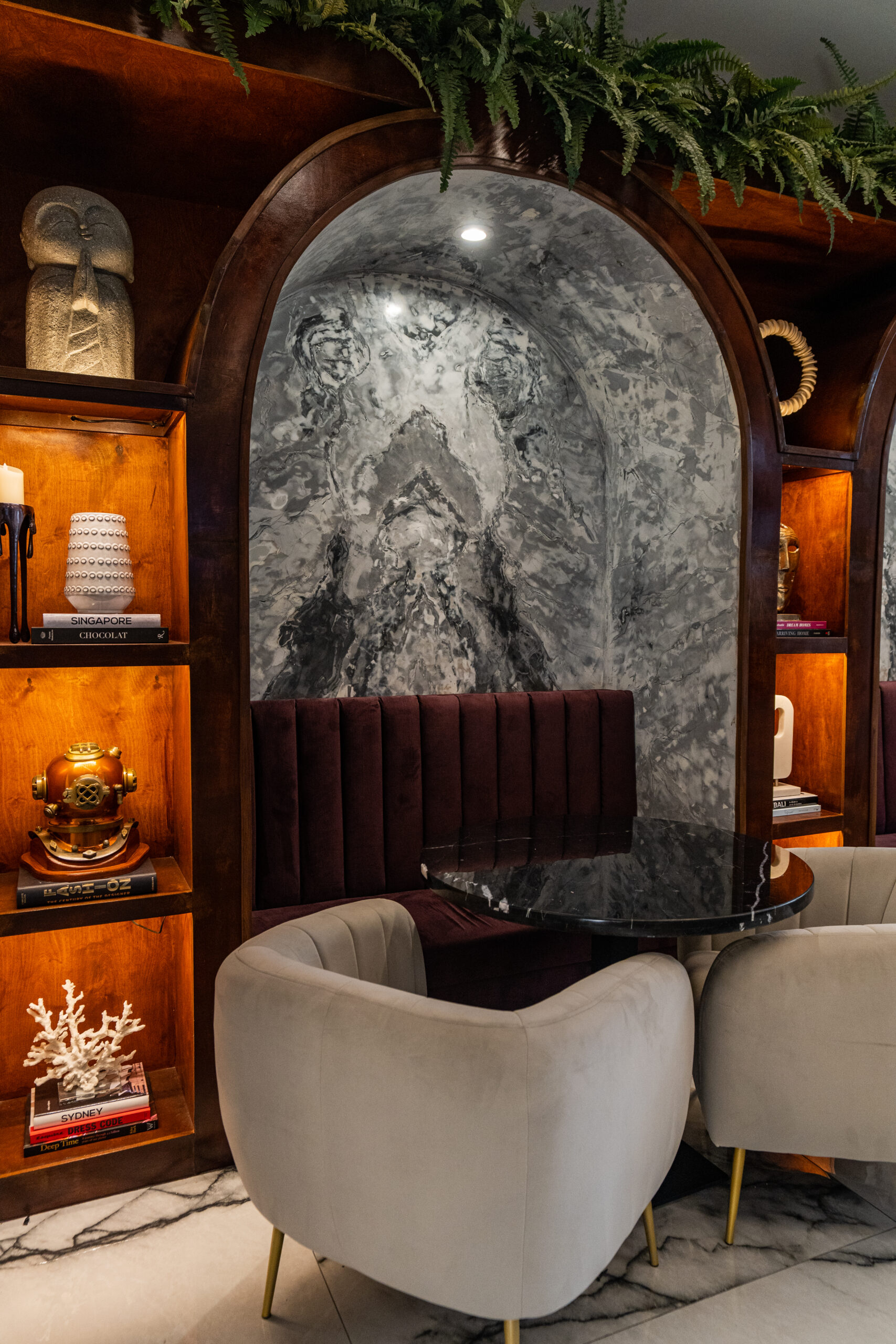 Arched banquette nook with built-in wood surround, marble table, upholstered seating, lounge chairs, and warm millwork
