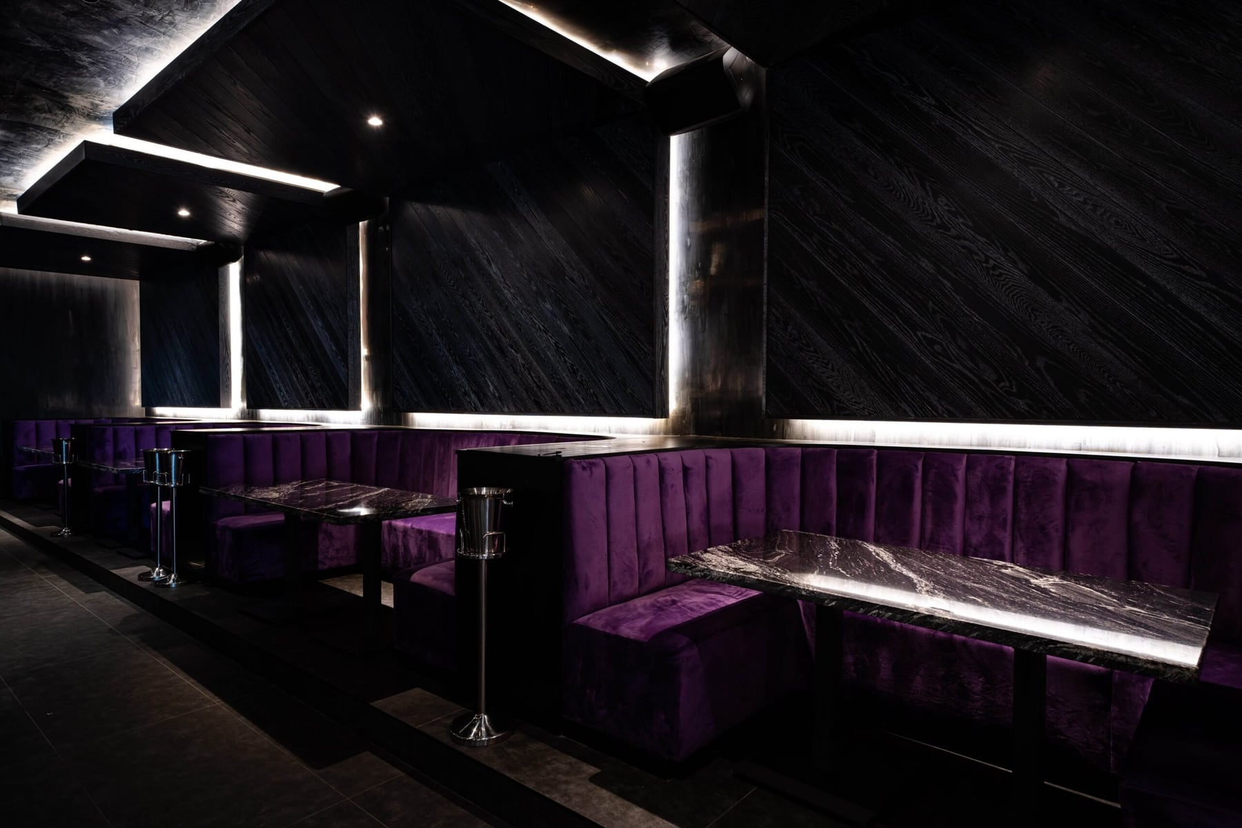 FRNDS Houston lounge with purple channel-tufted banquettes, marble tables, and dark wood wall panels