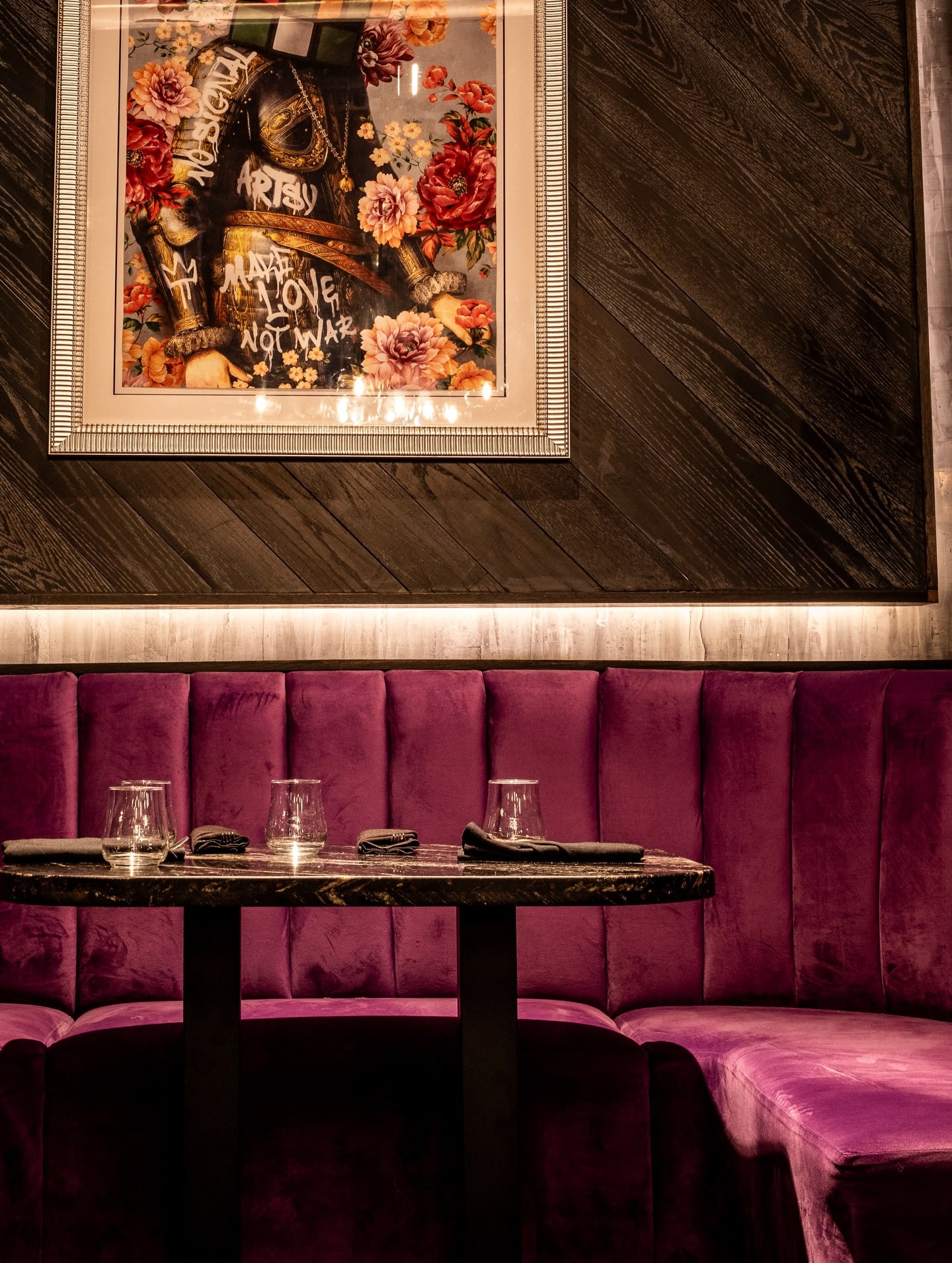 Purple upholstered booth with marble wall, black table, cream chairs, and brass table light