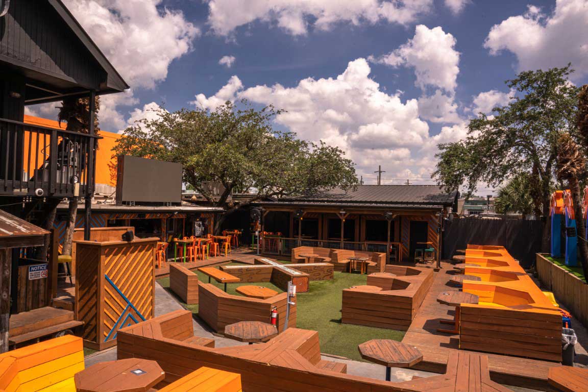KAMP Houston patio with built-in wood benches, patio tables, turf, and open-air restaurant seating