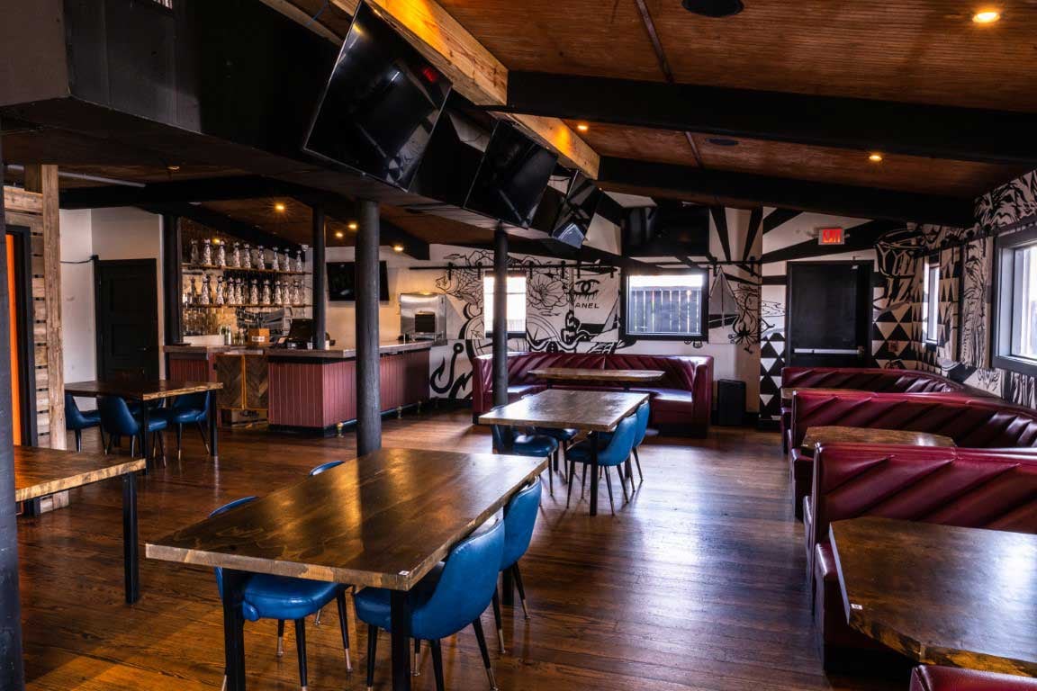 Indoor restaurant room with red booth seating, blue chairs, wood tables, bar, and service aisles