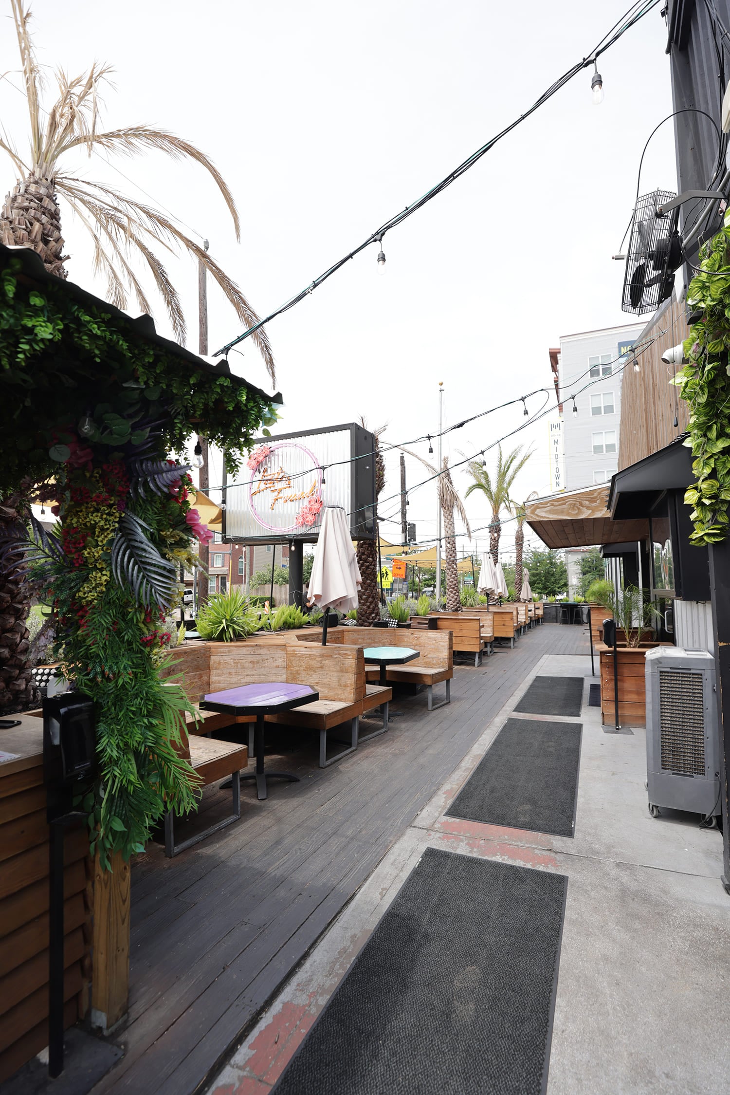 Outdoor patio with wood booth runs, small tables, string lights, and a narrow service aisle