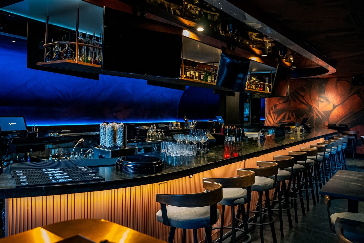 Thirteen Houston long bar with repeated bar stools, blue backlighting, and dark millwork
